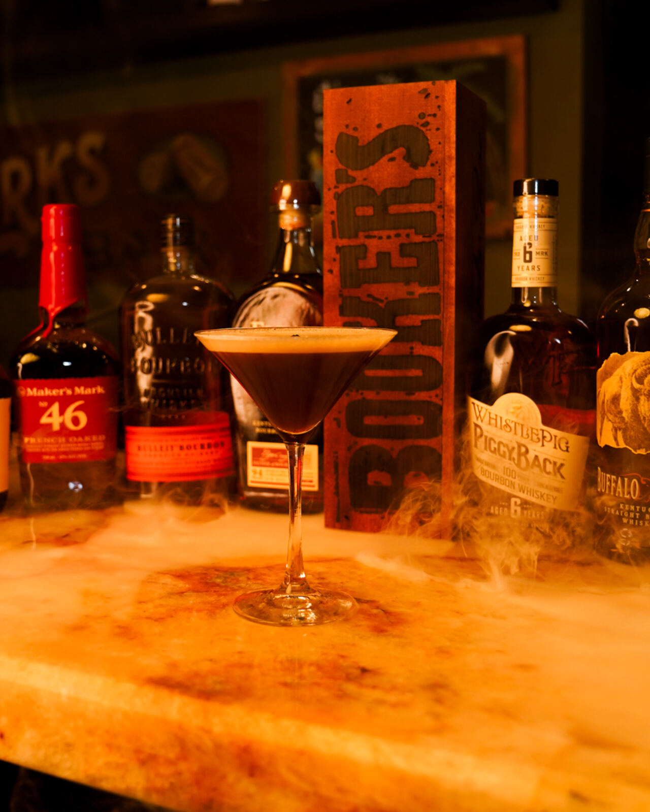 An espresso martini on the bar with the bourbon shelf behind